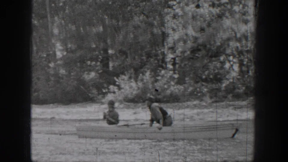 Chelan, Washington 1939 home-movie frame with two distant people seated in a small rowboat close to a tree-lined shore.