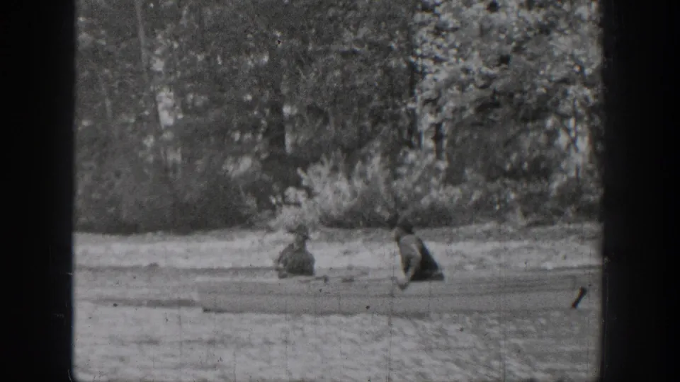 Black-and-white 8mm frame from Chelan, Washington showing two people in a rowboat on calm lake water beside dense trees.