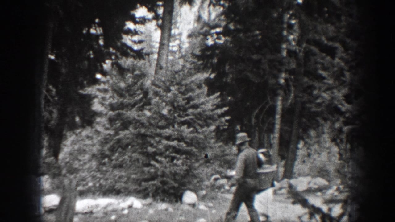 In Chelan, Washington home-movie footage from 1939, a man in a hat walks past rocks and pine trees in a wooded area.