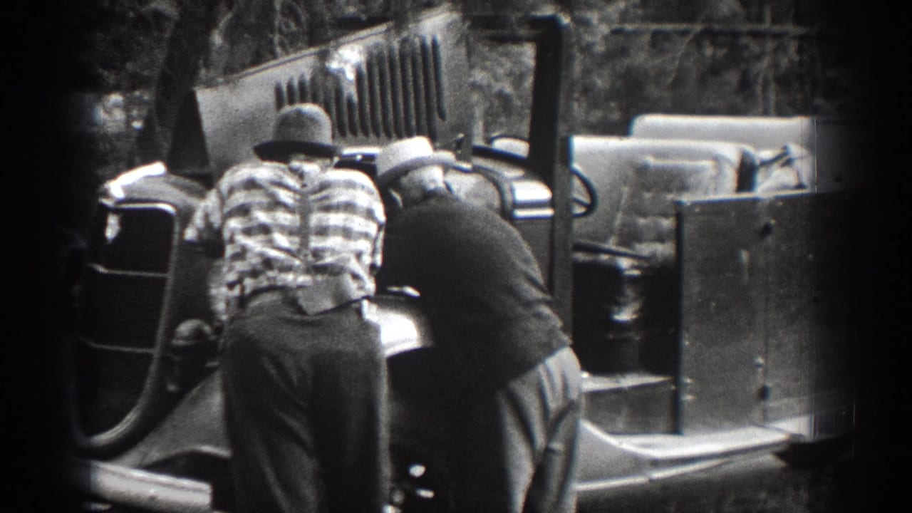 Two men, one in a plaid shirt and hat, lean near an older open vehicle in 1939 Chelan home-movie footage.