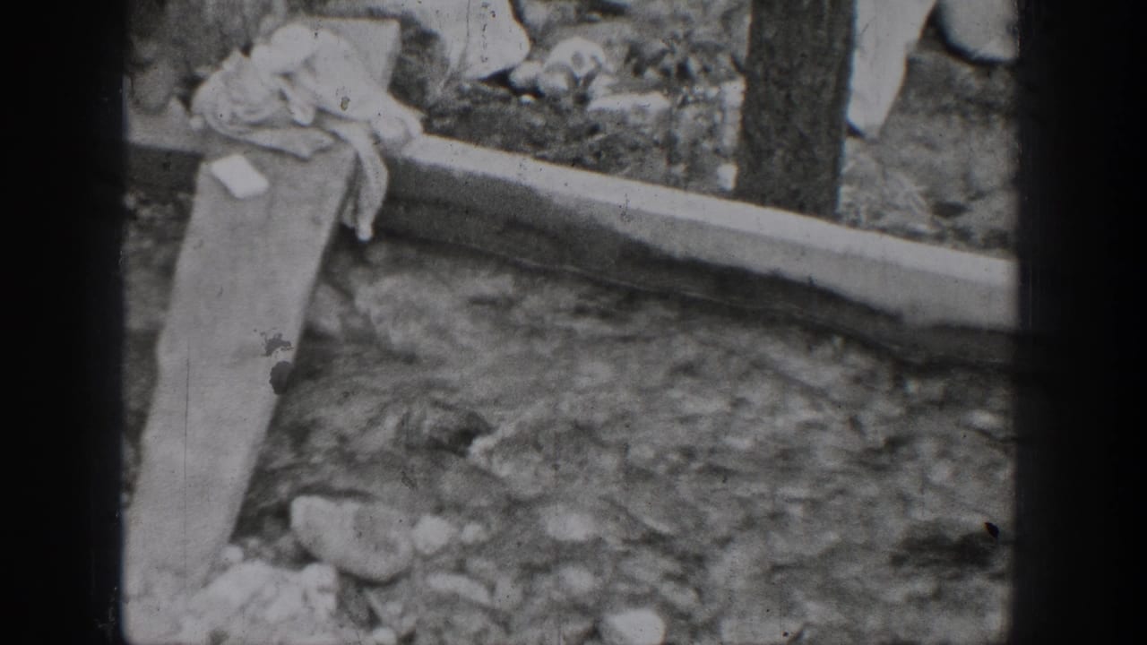 1939 Chelan, Washington home-movie frame showing a rocky stream, narrow wooden plank, and draped cloth near the bank.