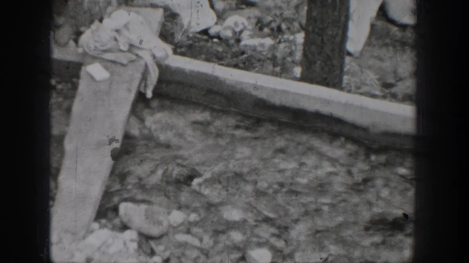 1939 Chelan, Washington home-movie frame showing a rocky stream, narrow wooden plank, and draped cloth near the bank.