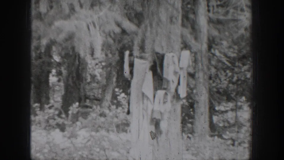 1939 Chelan home-movie frame showing a person in light clothing near trees and brush along the riverbank.