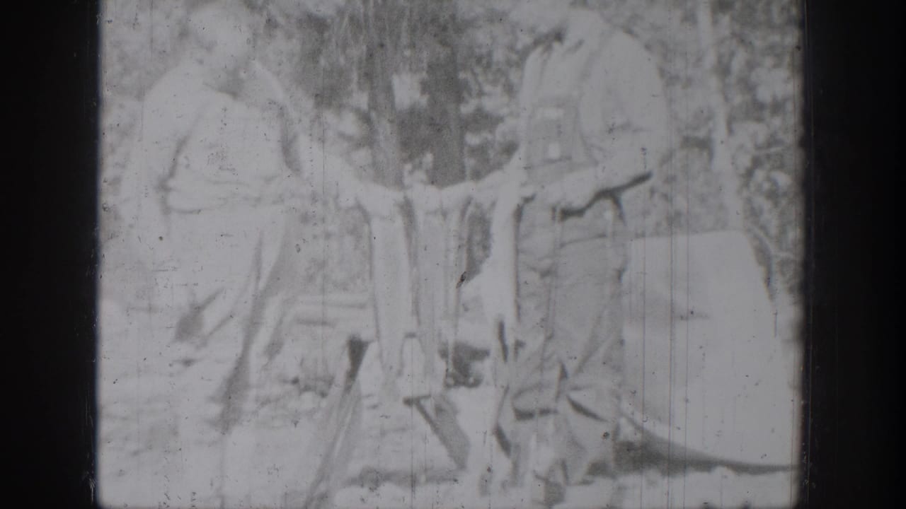 Washed-out 1939 home-movie frame of an older man and boy standing in the woods with fish held between them.