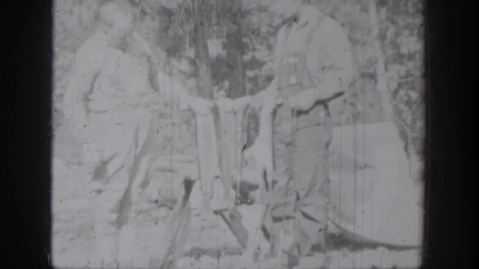 Washed-out 1939 home-movie frame of an older man and boy standing in the woods with fish held between them.