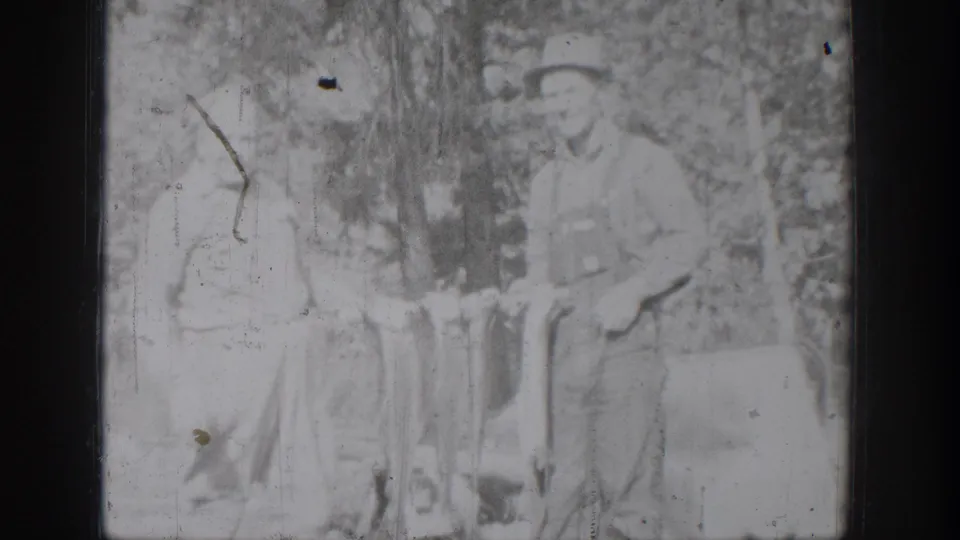 Chelan, Washington 8mm frame showing an older man in overalls and a boy beside a string of fish in a wooded area.