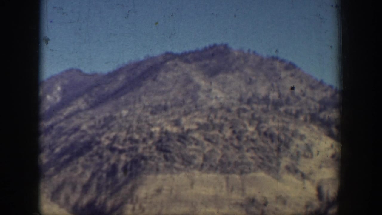 Soft 8mm view of a rugged mountain slope near Chelan, Washington, with lake-edge terrain visible through film grain.