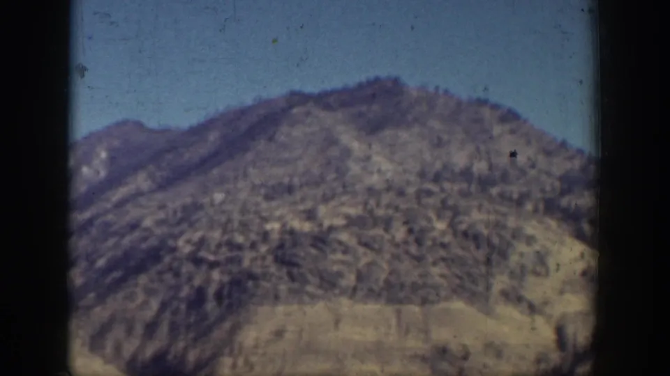 Soft 8mm view of a rugged mountain slope near Chelan, Washington, with lake-edge terrain visible through film grain.