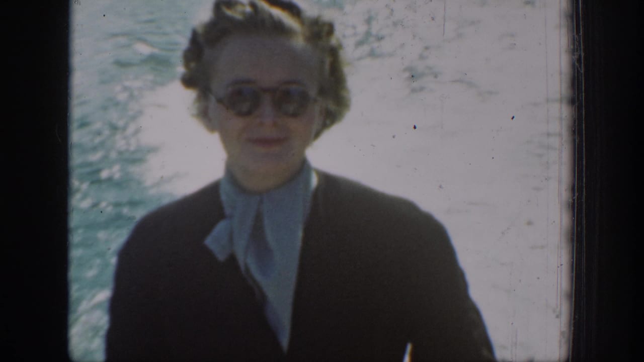 1939 Chelan, Washington frame showing a woman facing the camera in sunglasses, a dark jacket, and a light scarf on a boat.
