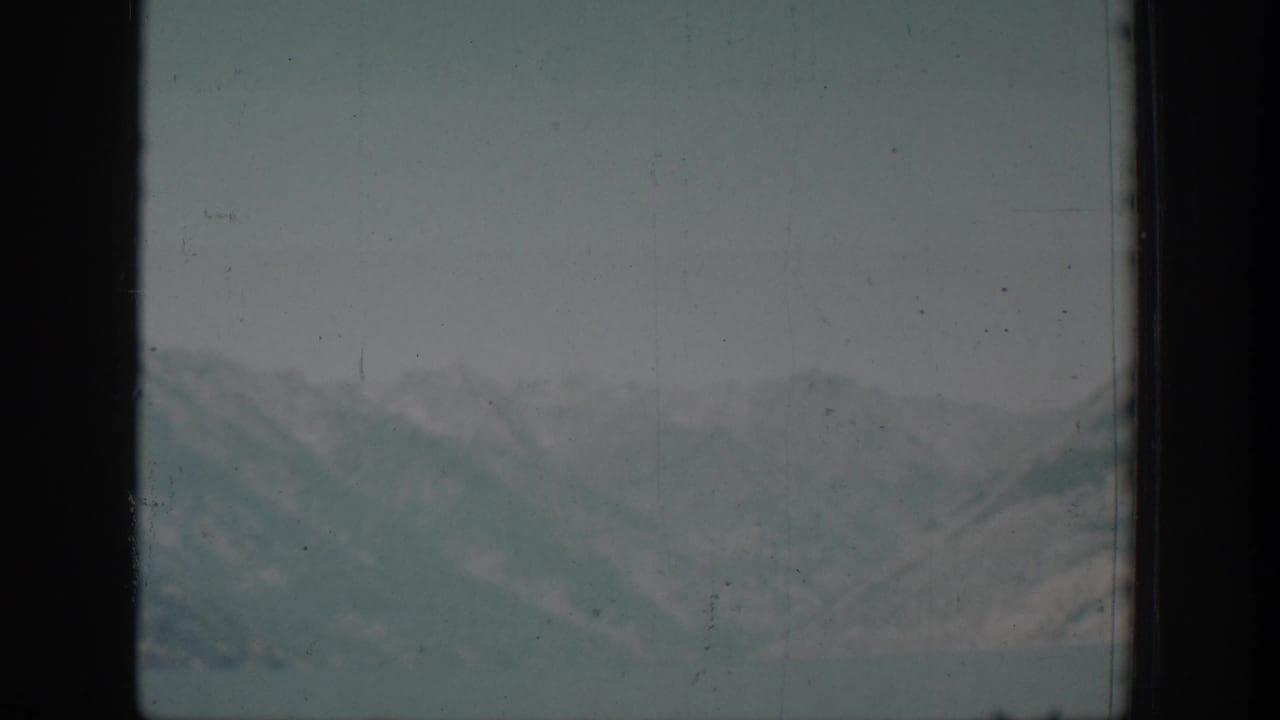 Chelan-area mountain ridges appear through a dark window frame in faded 1939 8mm travel footage.