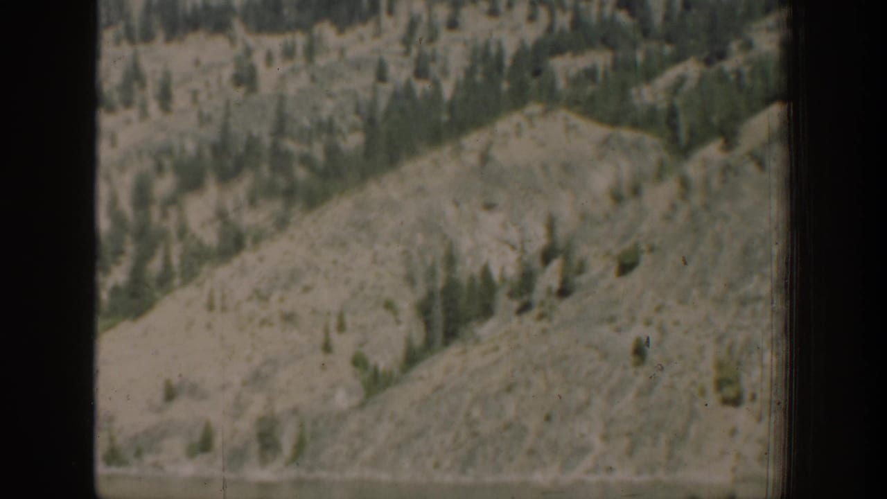 Rocky and forested Chelan-area hillside above water, seen through a vehicle window in 1939 home-movie footage.