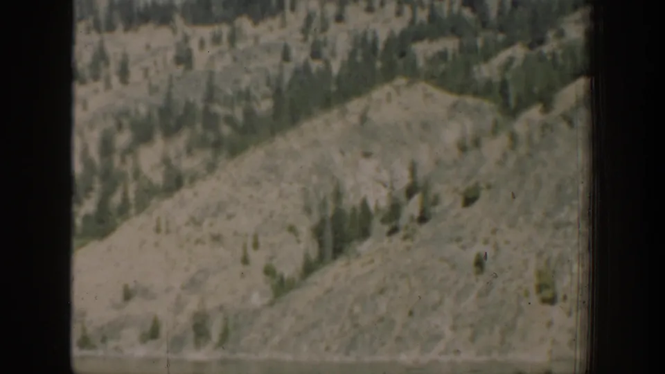 Rocky and forested Chelan-area hillside above water, seen through a vehicle window in 1939 home-movie footage.