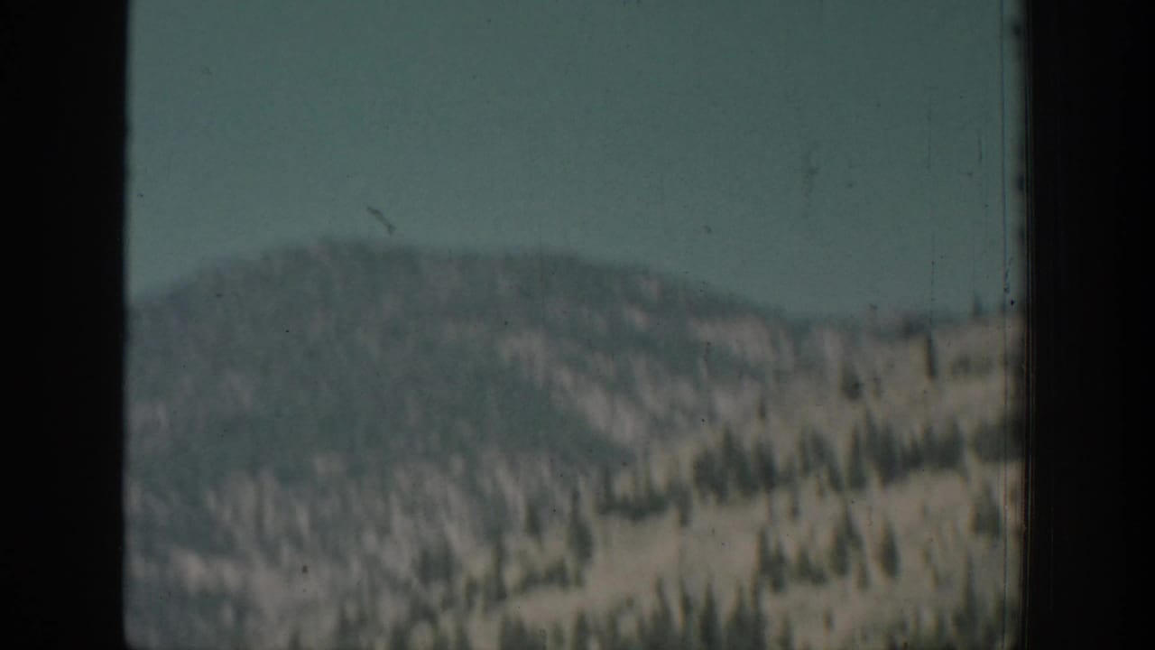 Soft mountain hillside seen through a dark window frame under blue sky.