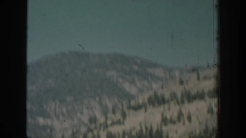 1939 Chelan, Washington home-movie frame showing a distant tree-dotted hillside viewed through a dark window edge.