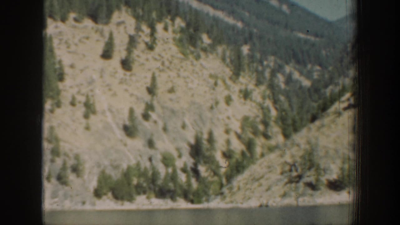 Chelan-area mountain slope in 1939 8mm footage, with pale exposed ground and scattered evergreens framed by a dark interior edge.