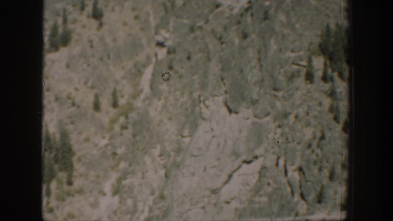 A closer 1939 Chelan, Washington view of rough hillside terrain, brush, and scattered trees, softened by 8mm film grain.