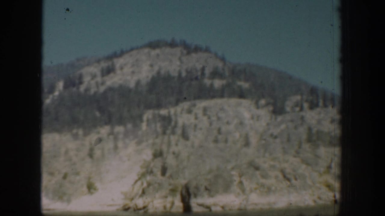 1939 Chelan, Washington mountain view through a dark window opening, showing a rounded slope with scattered trees beneath clear sky.