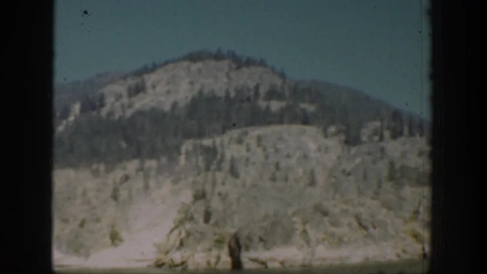 1939 Chelan, Washington mountain view through a dark window opening, showing a rounded slope with scattered trees beneath clear sky.