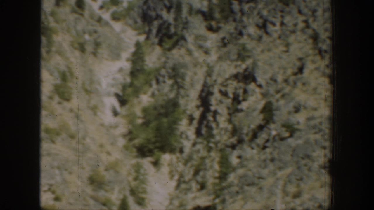 1939 Chelan-area mountain slope with rocks, dry grass, a narrow path, and scattered evergreens in soft 8mm color.