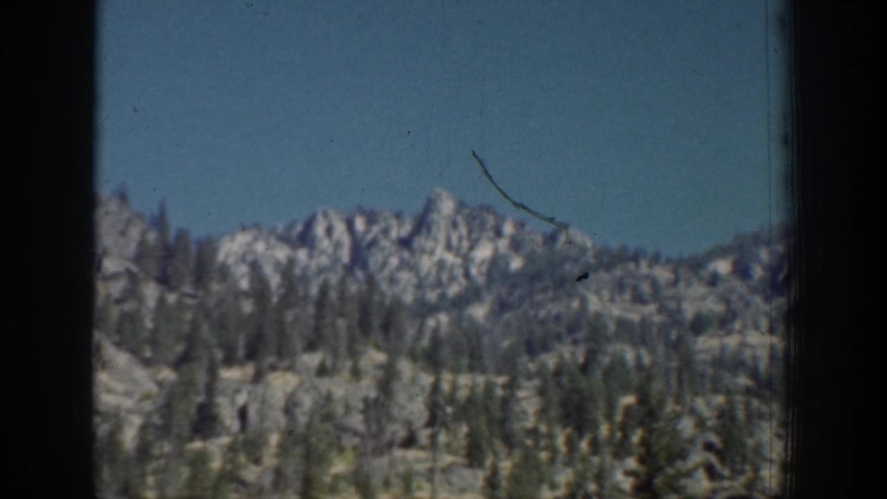 1939 Chelan-area landscape with jagged mountain ridges, evergreen forest, and clear blue sky in grainy 8mm footage.