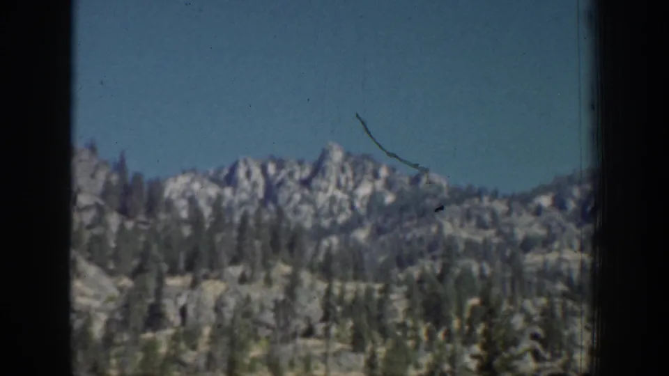 1939 Chelan-area landscape with jagged mountain ridges, evergreen forest, and clear blue sky in grainy 8mm footage.