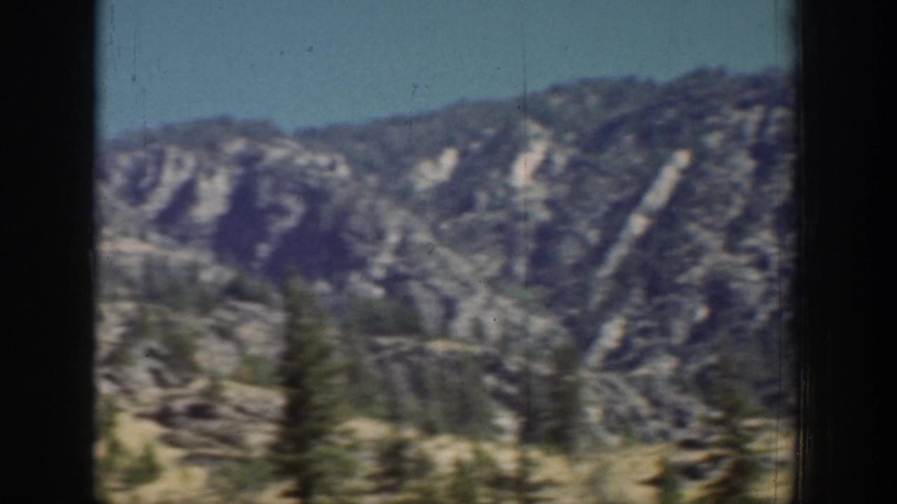 Chelan-area mountain vista with layered ridges, scattered evergreens, rocky slopes, and soft motion blur from vintage 8mm film.
