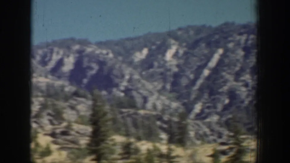 Chelan-area mountain vista with layered ridges, scattered evergreens, rocky slopes, and soft motion blur from vintage 8mm film.