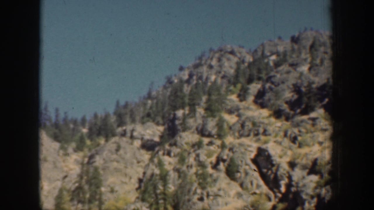 Vintage 8mm view of a steep Chelan-area rocky slope with scattered trees and a dark vertical frame edge.