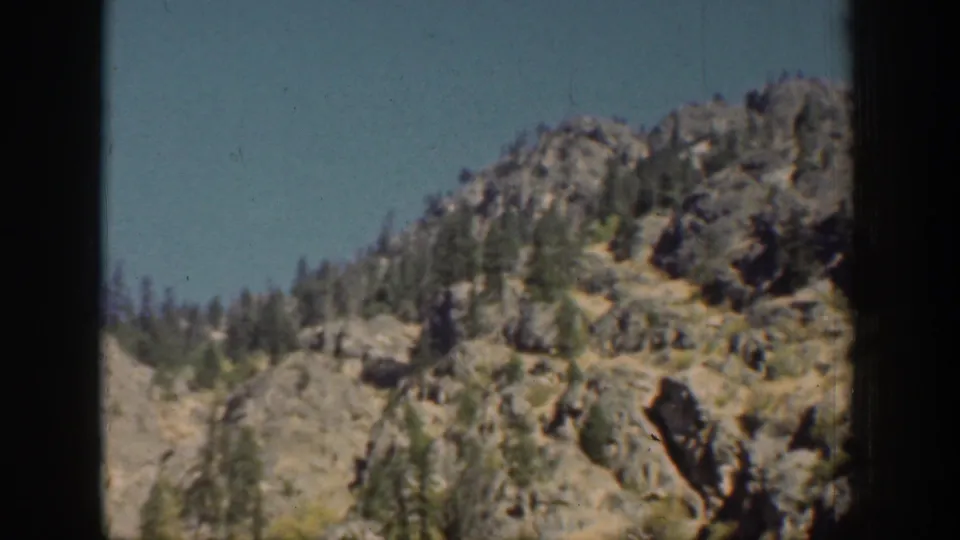 Vintage 8mm view of a steep Chelan-area rocky slope with scattered trees and a dark vertical frame edge.