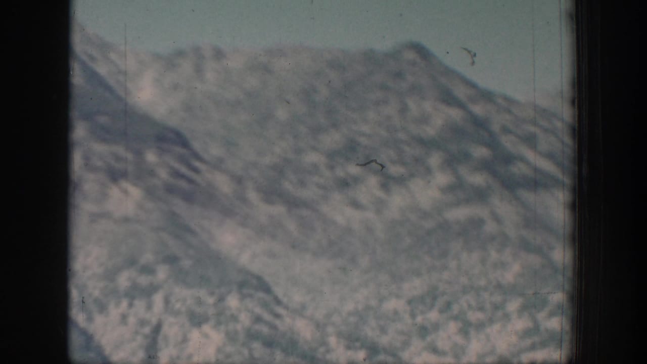 Faded 8mm frame of a distant mountain face near Chelan, softened by age, exposure, and visible film wear.