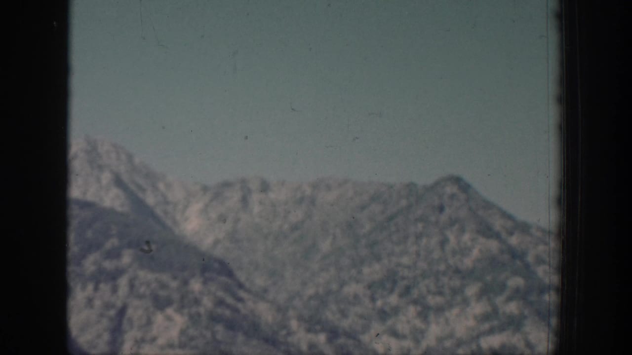 Distant rocky mountain ridges under pale sky, framed by dark vertical edges.