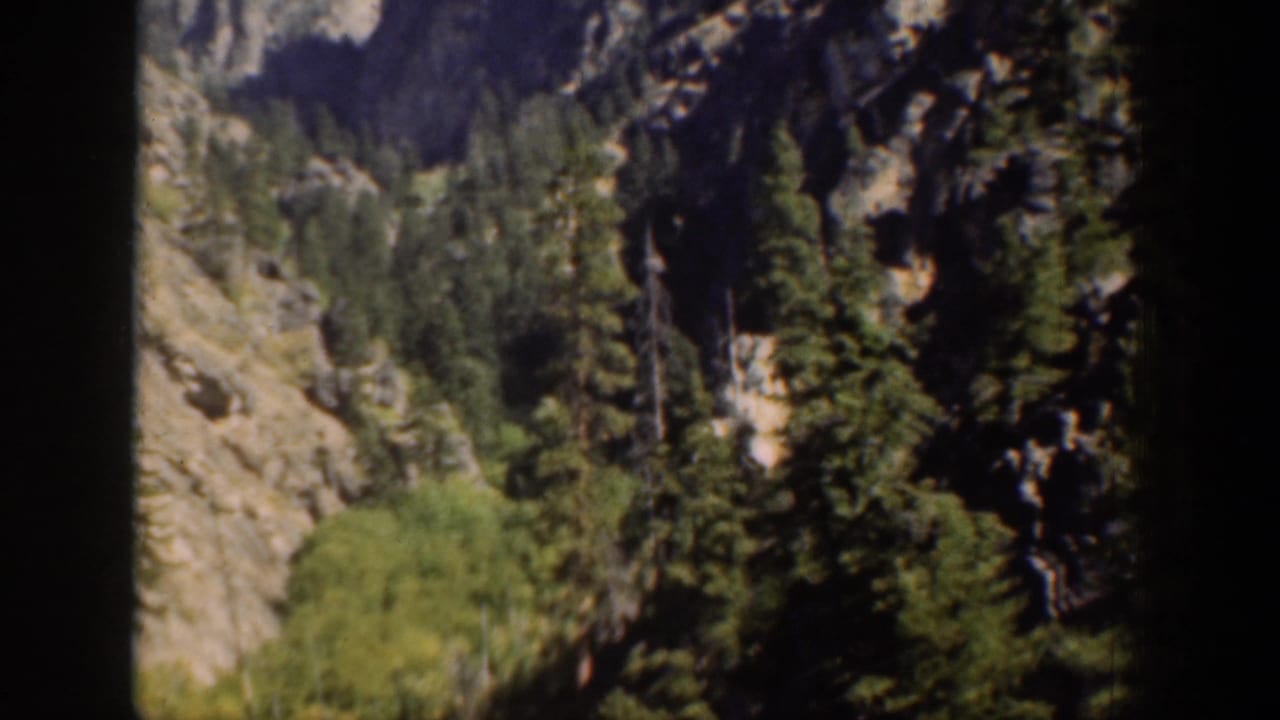 Chelan-area mountain scenery appears as a steep rocky canyon wall with trees and brush, filmed in soft 8mm color.