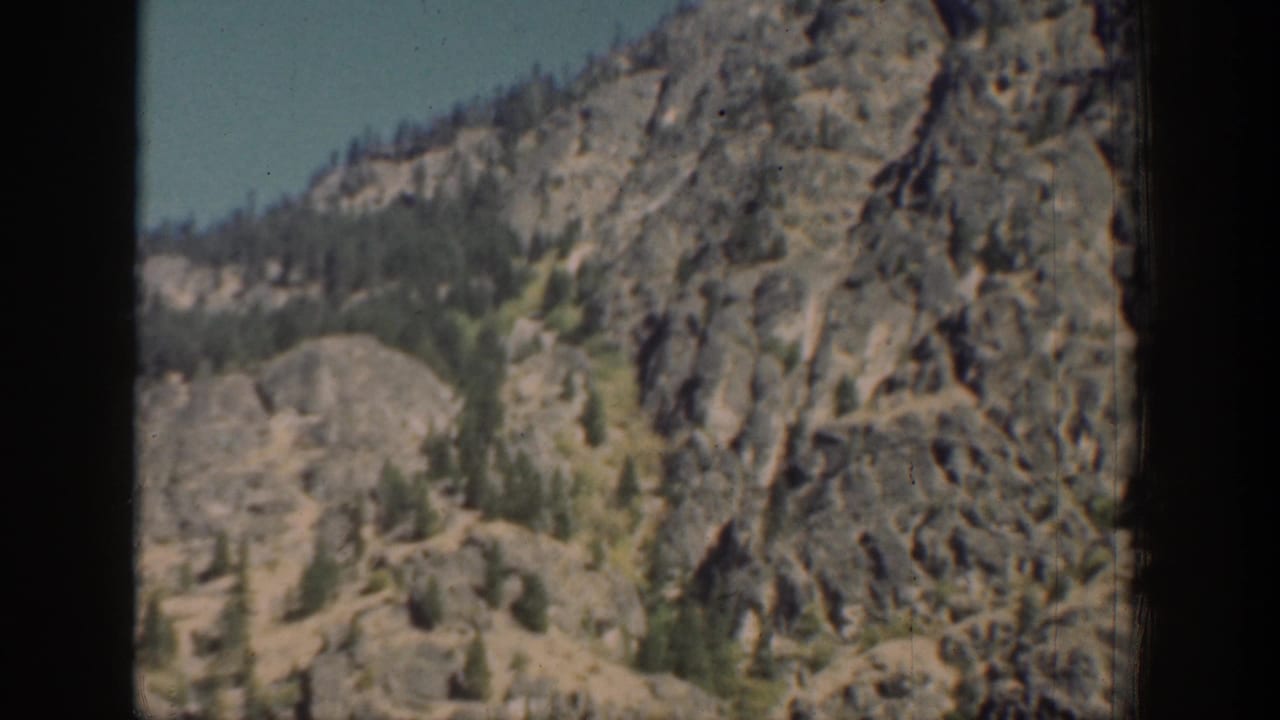 Vintage 8mm view of a rocky Chelan mountainside with sparse trees, pale sky, and dark window-like framing.