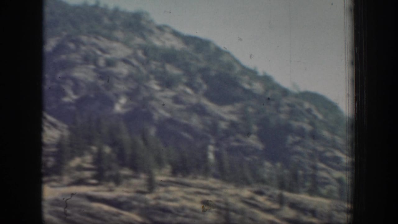 Faded 1939 home-movie frame showing a distant tree-dotted mountain slope in Chelan, Washington, bordered by dark film or window edges.
