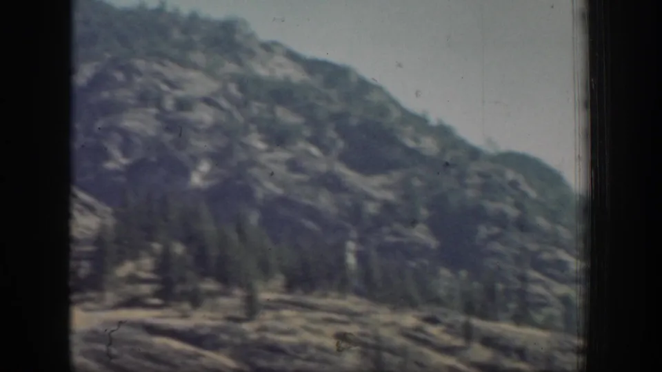 Faded 1939 home-movie frame showing a distant tree-dotted mountain slope in Chelan, Washington, bordered by dark film or window edges.