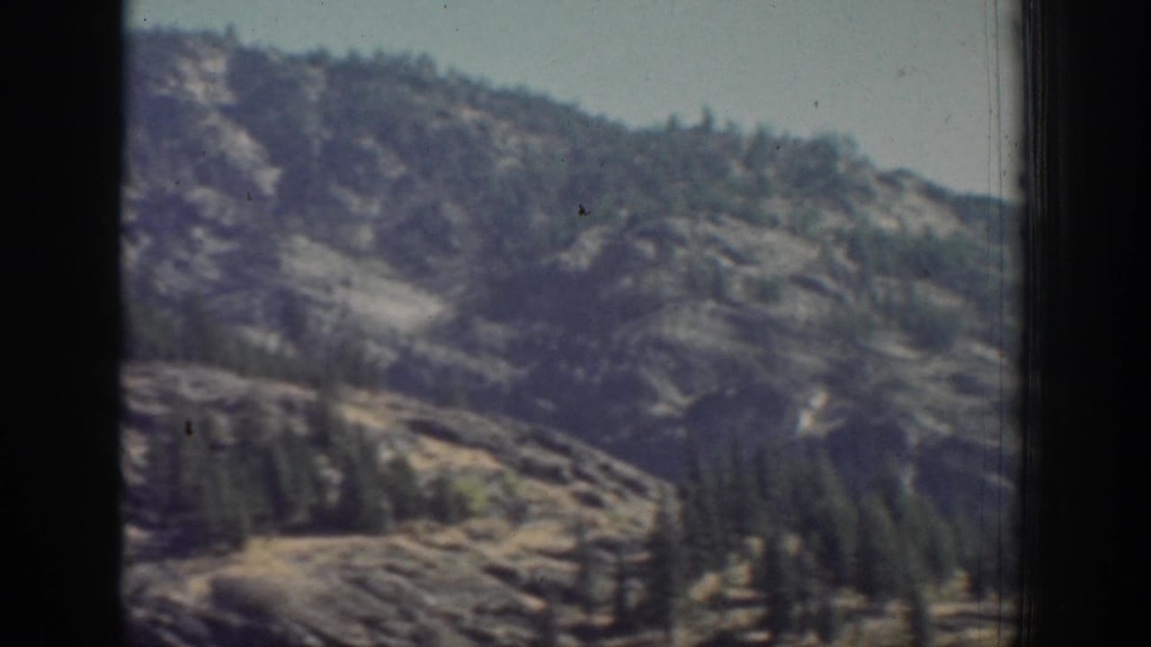 Rocky mountain slope and evergreens seen through dark window framing.
