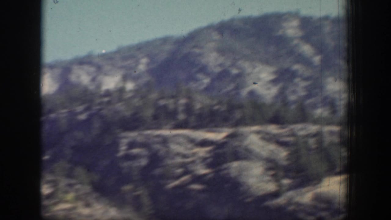 Chelan-area mountain terrain appears in soft focus through a vehicle window, with dry rock faces and scattered trees.
