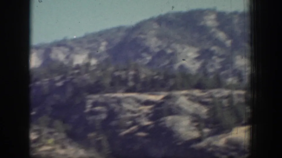 Chelan-area mountain terrain appears in soft focus through a vehicle window, with dry rock faces and scattered trees.