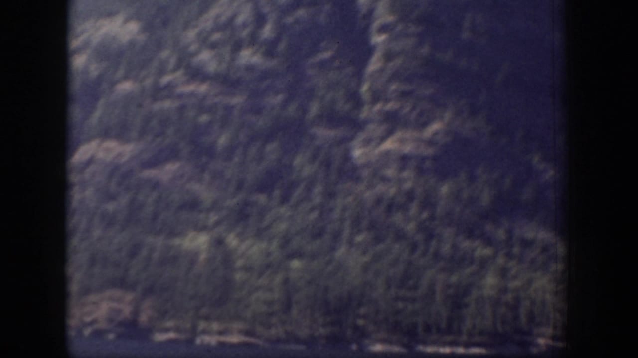 A dimmer 8mm frame shows steep rocky terrain and conifers passing outside a window in Chelan, Washington.