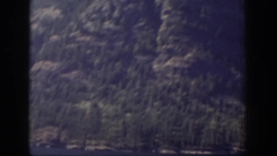 A dimmer 8mm frame shows steep rocky terrain and conifers passing outside a window in Chelan, Washington.