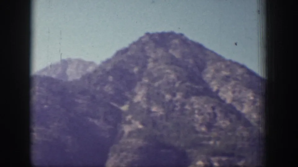 1939 Chelan, Washington frame with a rounded mountain peak, distant ridge, and clear blue sky in soft color film.