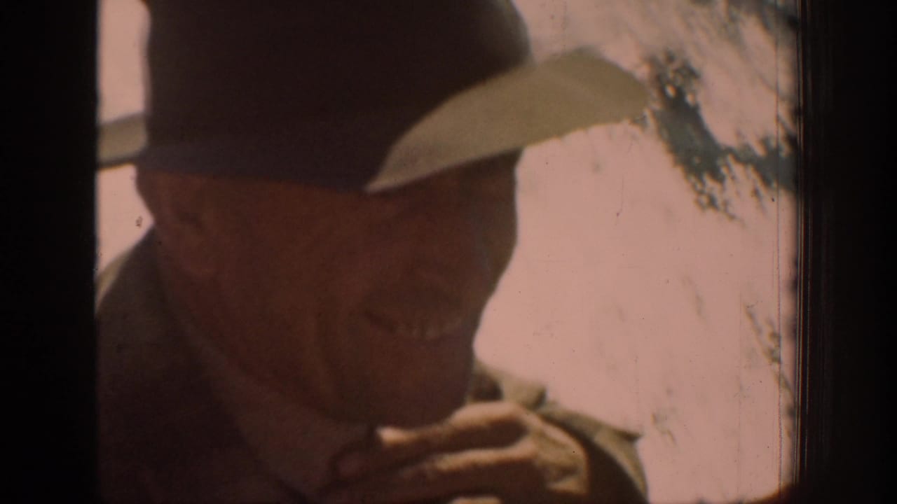 In 1939 Chelan home-movie footage, an adult man in a brimmed hat rubs his chin near a window in warm, soft light.