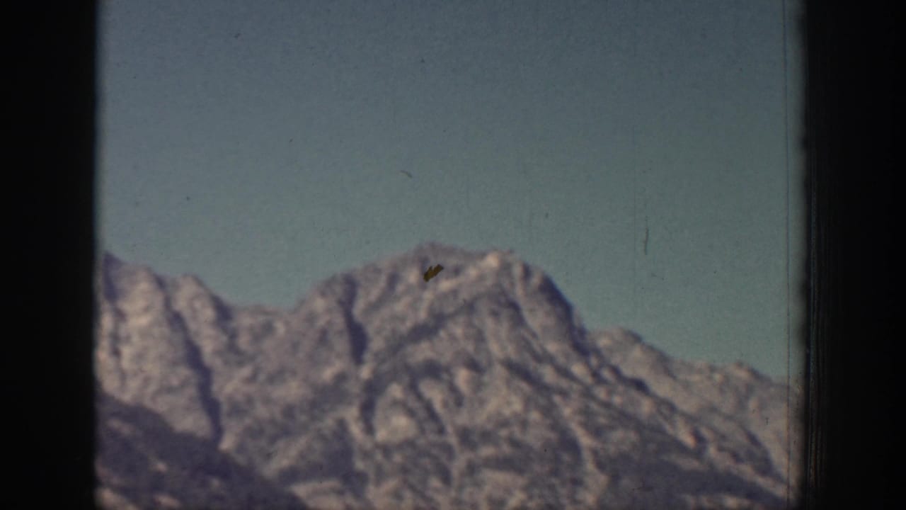A rocky, snow-marked mountain peak fills the lower frame under blue sky in the 1939 Chelan home movie.