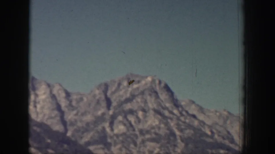 A rocky, snow-marked mountain peak fills the lower frame under blue sky in the 1939 Chelan home movie.