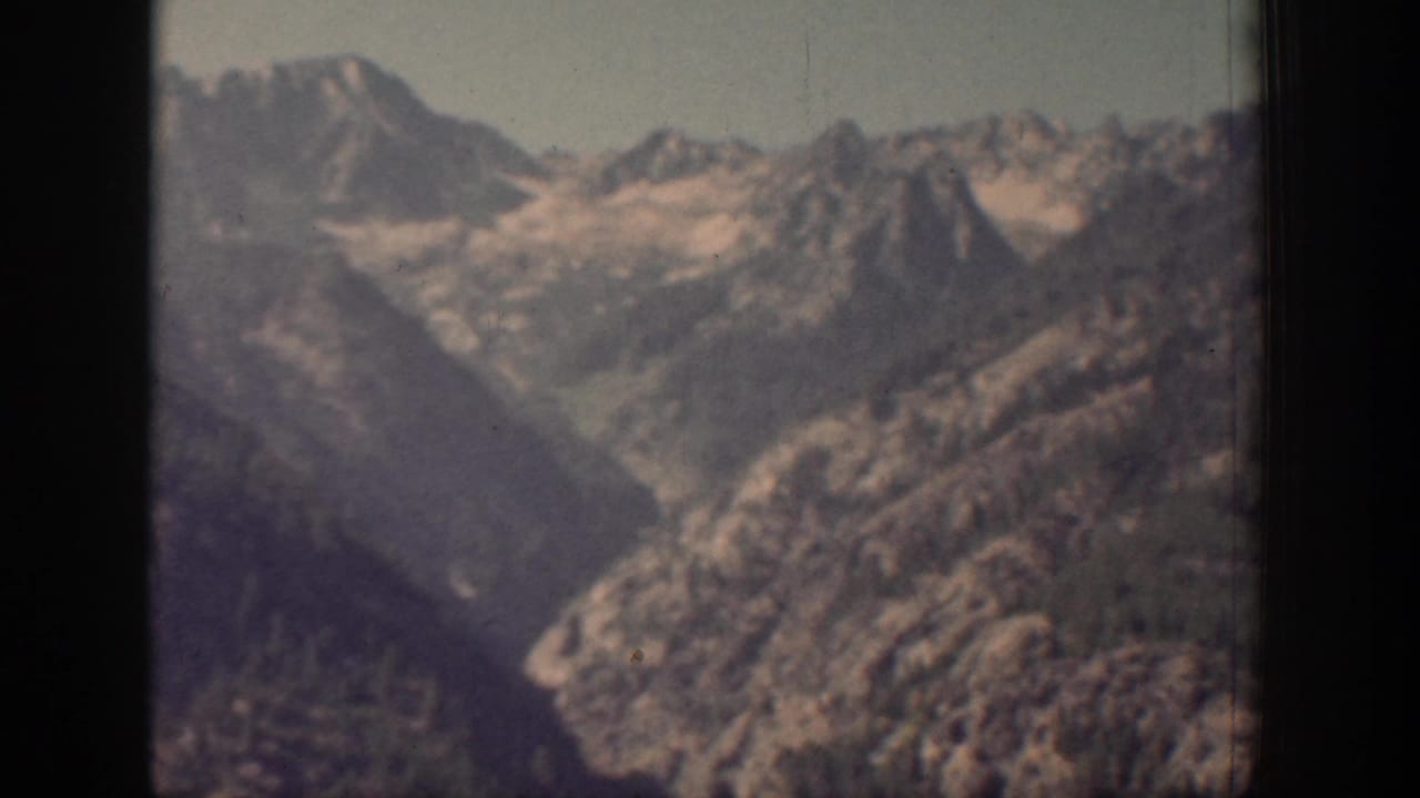 1939 Chelan, Washington home-movie frame showing distant rocky mountain ridges under a clear pale sky, softened by grain and focus.