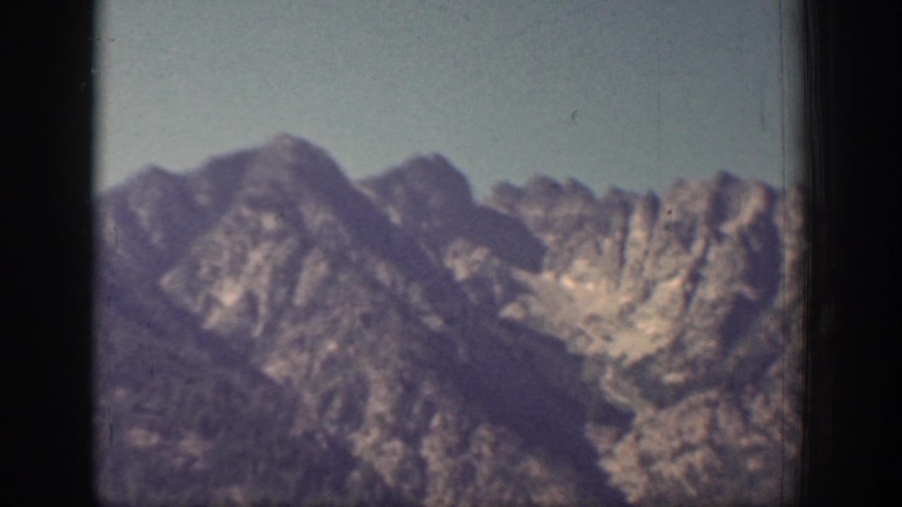 Chelan-area mountain ridges appear in a soft 1939 8mm frame, with pale sky and a dark vertical gate edge visible.