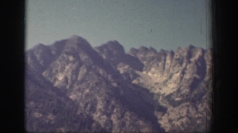 Chelan-area mountain ridges appear in a soft 1939 8mm frame, with pale sky and a dark vertical gate edge visible.