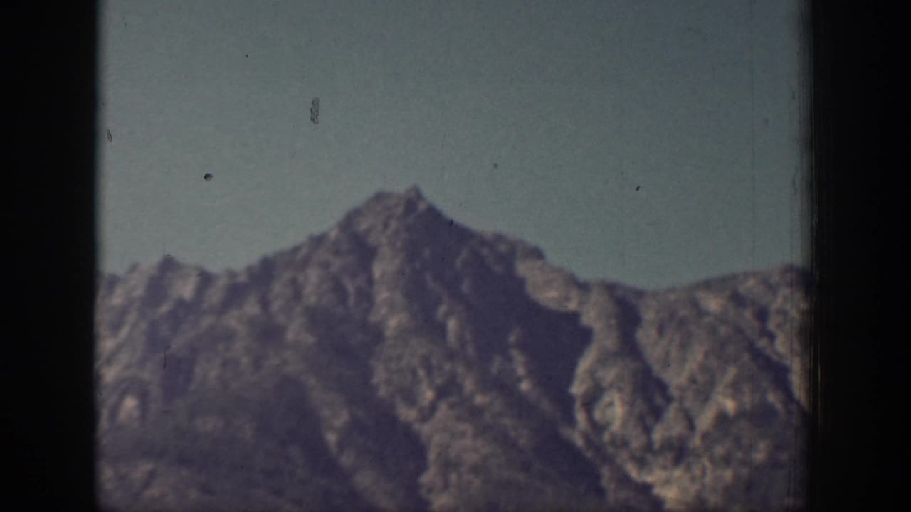 Rugged mountain peaks under a pale sky with dark film borders.