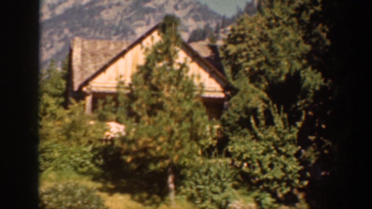 1939 Chelan-area 8mm frame showing a rustic wooden cabin among trees with a mountain backdrop.