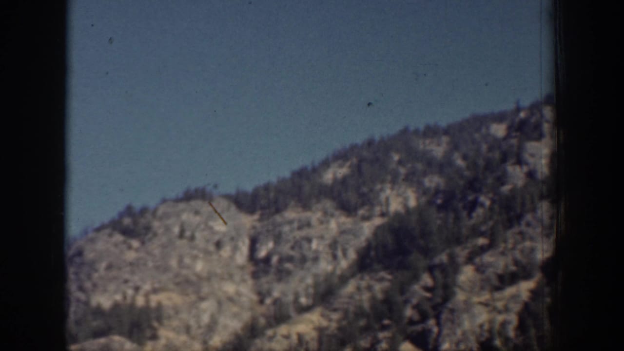 Vintage 8mm view of a Chelan-area rocky outcrop with scattered evergreens and open sky.